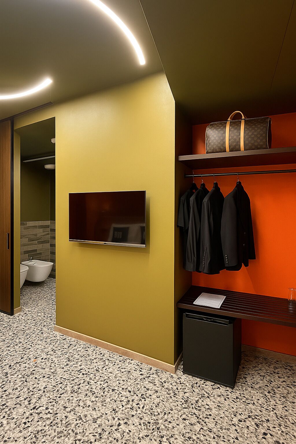 A modern bathroom with a large mirror, a towel rack with black towels, a suitcase on a shelf, and a toilet with a bidet.