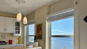 A kitchen with a cart, a chair by the window, and a view of the sea.