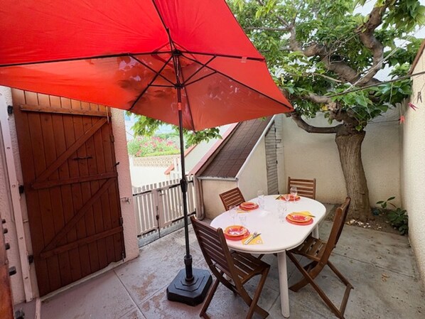 An outdoor patio with a table set for two, an umbrella, and a wooden gate.