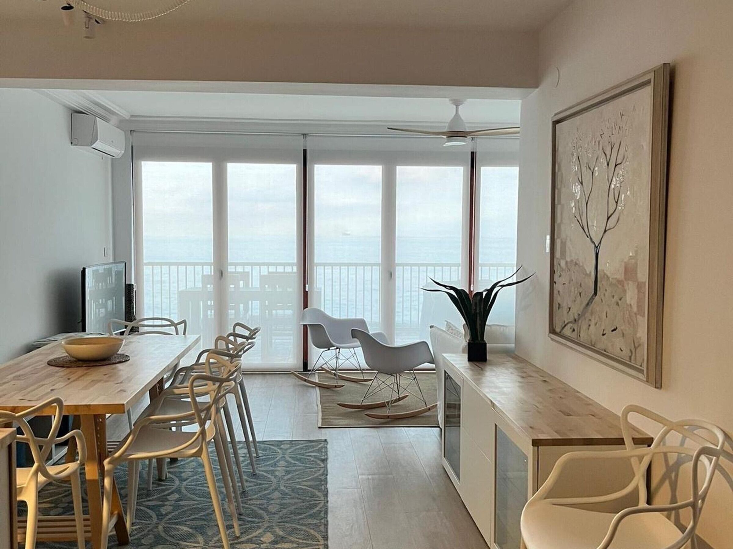 Un espace repas moderne avec une table en bois, plusieurs chaises, un téléviseur et un balcon offrant une vue.