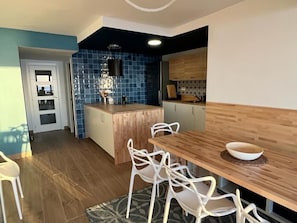 Cocina moderna con baldosas azules, armarios de madera y un comedor con mesa de madera y sillas blancas.