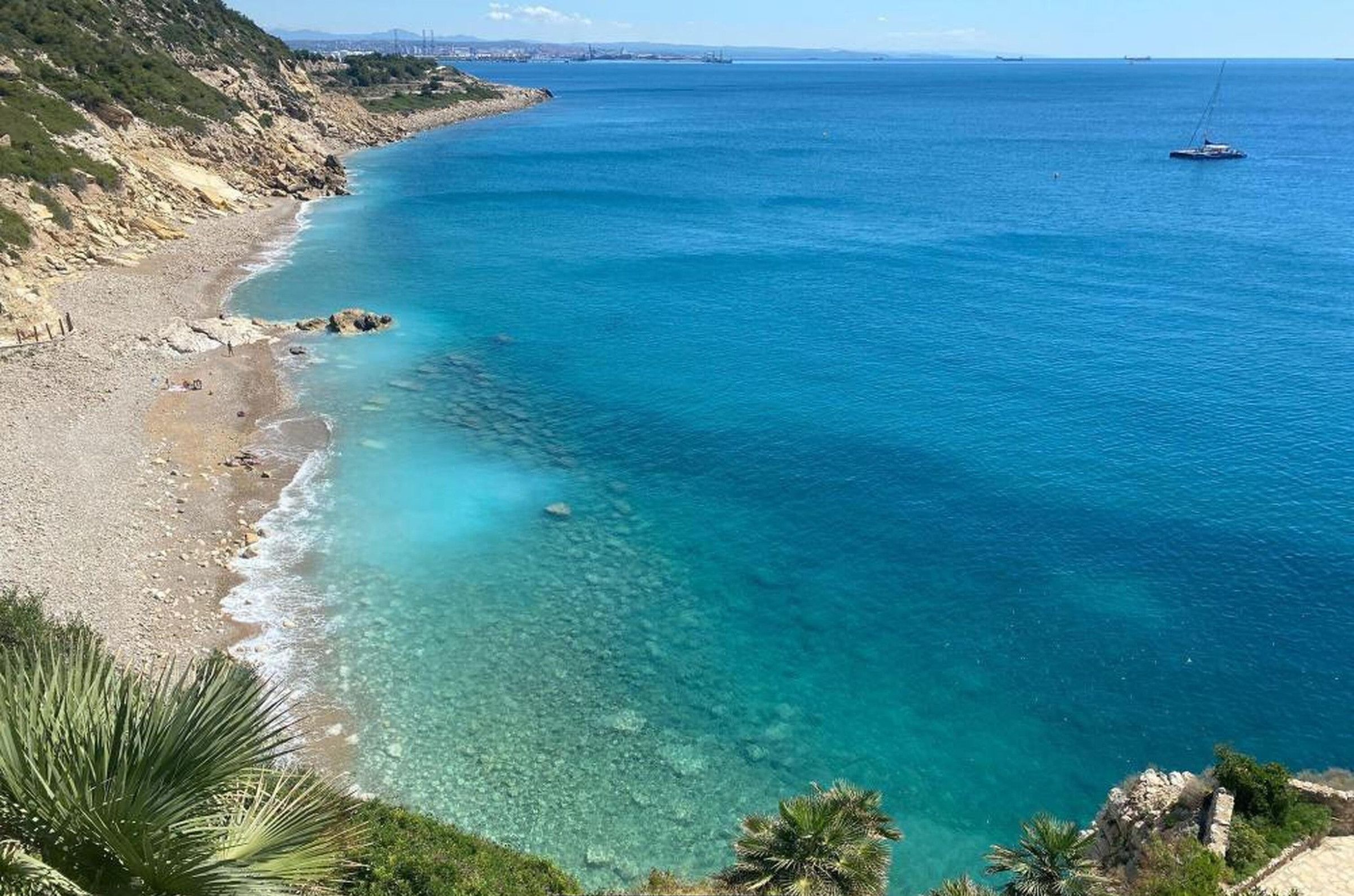 Uitzicht op de kust met een heldere blauwe zee, een zandstrand en een bord waarop 'DOMium Costa Pinos Mar' staat.