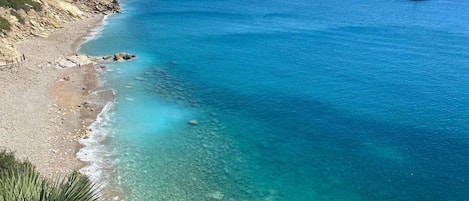 Vista costeira com mar azul cristalino, praia de areia e um sinal indicando 'DOMium Costa Pinos Mar'.