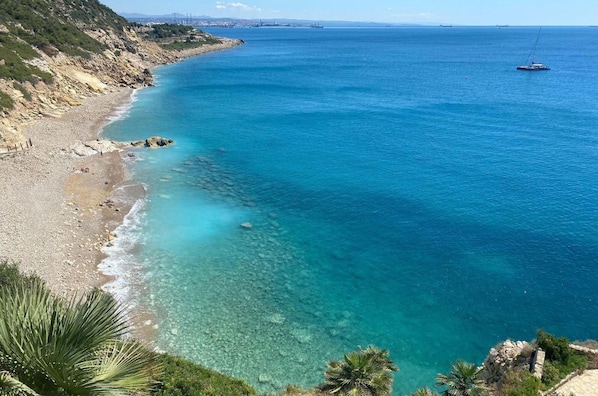 A coastal view with a clear blue sea, a sandy beach, and a sign indicating 'DOMium Costa Pinos Mar'.