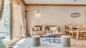A cozy living room with a sofa, ottomans, a dining table, and a chandelier. - Champagny en Vanoise - Premium Apartment 6 ppl, Terrace, WIFI, Parking (Champagny-en-Vanoise)