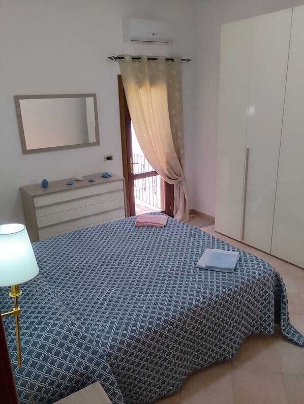 A bedroom with a bed, a bedside table, a mirror, a wardrobe, and a window with curtains.
