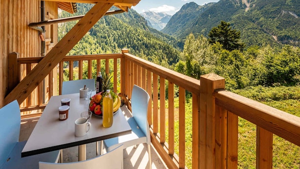 Une terrasse en bois avec une table dressée pour deux personnes, offrant une vue sur un paysage montagneux.