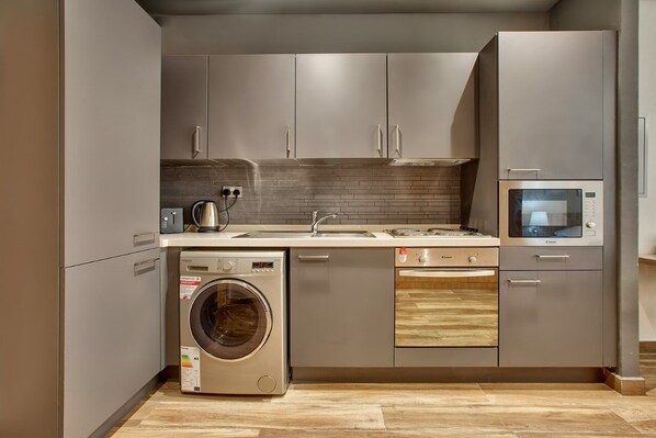 Una cocina moderna con gabinetes grises, lavadora integrada, microondas y lavavajillas.