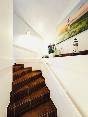 Eine Treppe mit dunkelbraunen Fliesen, die zu einer Zwischenebene mit einem weißen Geländer führt.