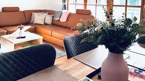 A modern living room with a sofa, coffee table, and a dining area with a vase of flowers. - Cozy vacation home between lake, forest and sea (Scharbeutz)