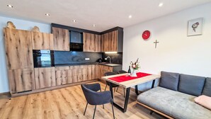 Une cuisine moderne avec des meubles en bois, un coin repas agrémenté d’un chemin de table rouge et un canapé gris.