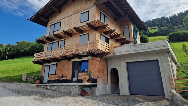 Une maison en bois à deux étages, dotée d’un balcon, d’un garage et d’une pelouse bien entretenue.