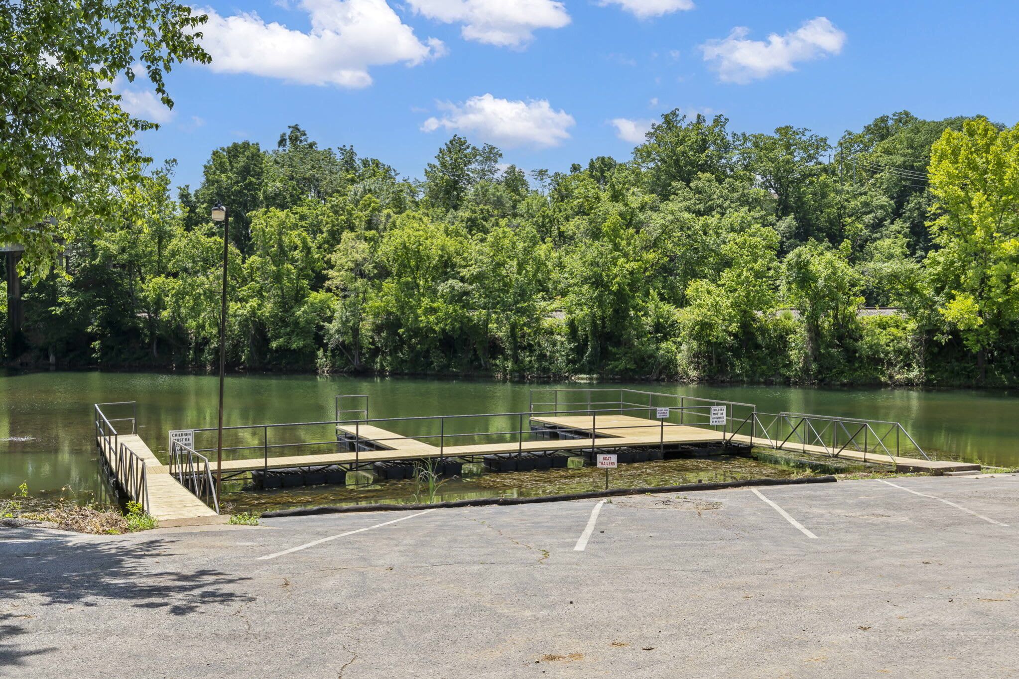 A parking lot with a dock extending into a lake, surrounded by dense trees.