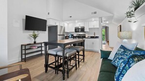 A modern kitchen with white cabinets, a black countertop, and a built-in oven. There is a dining area with a wooden table and bar stools. - Creek View Near the Landing (Branson)