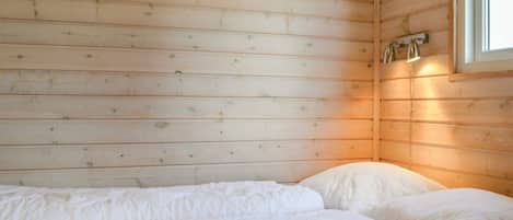 Quarto com teto de ripas de madeira, cama com roupa de cama branca e janela com luminária.