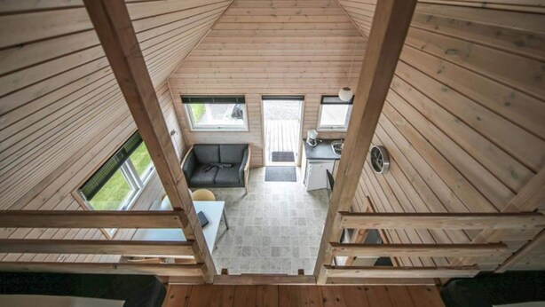 Eine Holzhütte mit hohen Decken, einem Schlafzimmer im oberen Bereich, einem Essbereich und einer Küche.