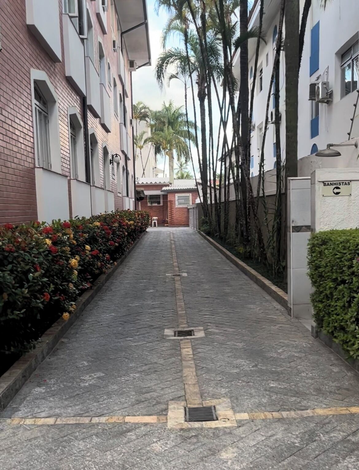 Un sendero estrecho y empedrado bordeado por edificios con fachadas de ladrillo y blanco, que conduce a un edificio con un cartel que dice "BANHISTAS".