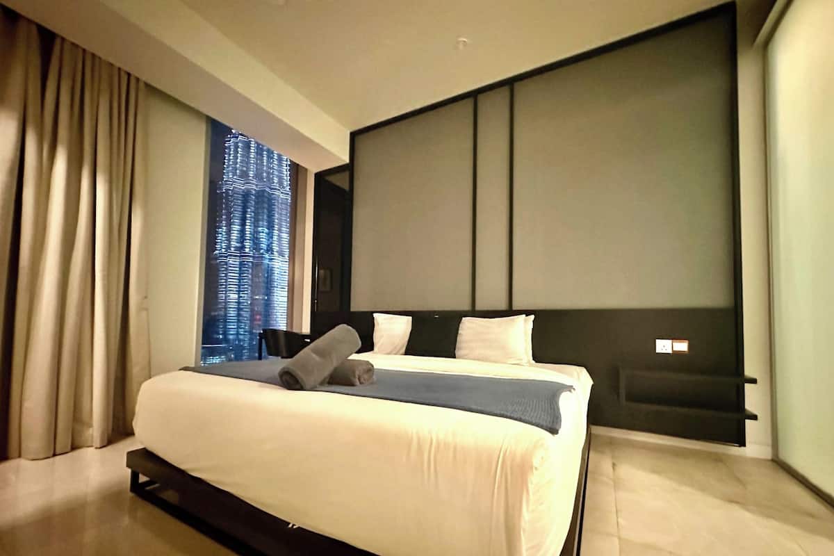 Ein modernes Hotelzimmer mit einem großen Bett, einer Kopfteil und Blick auf die Stadt durch das Fenster.