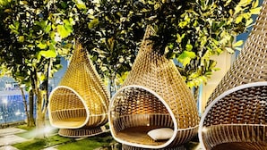 Three wicker hanging chairs with circular openings, placed on a tiled patio with a view of a cityscape. - TropicanaThe Residence KLCC By Cozy Stay (Kuala Lumpur)
