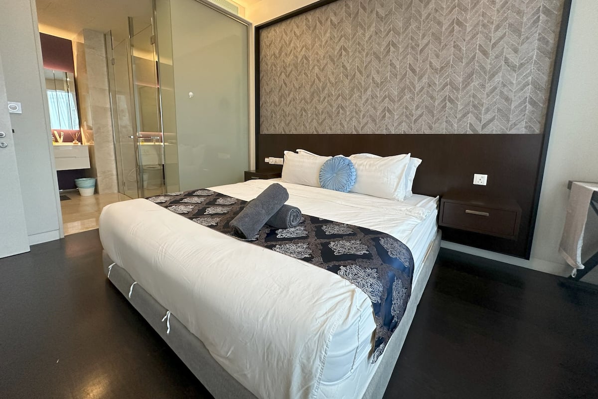 Ein modernes Hotelzimmer mit einem großen Bett, einem begehbaren Kleiderschrank und einem Badezimmer mit einer Glasdusche.