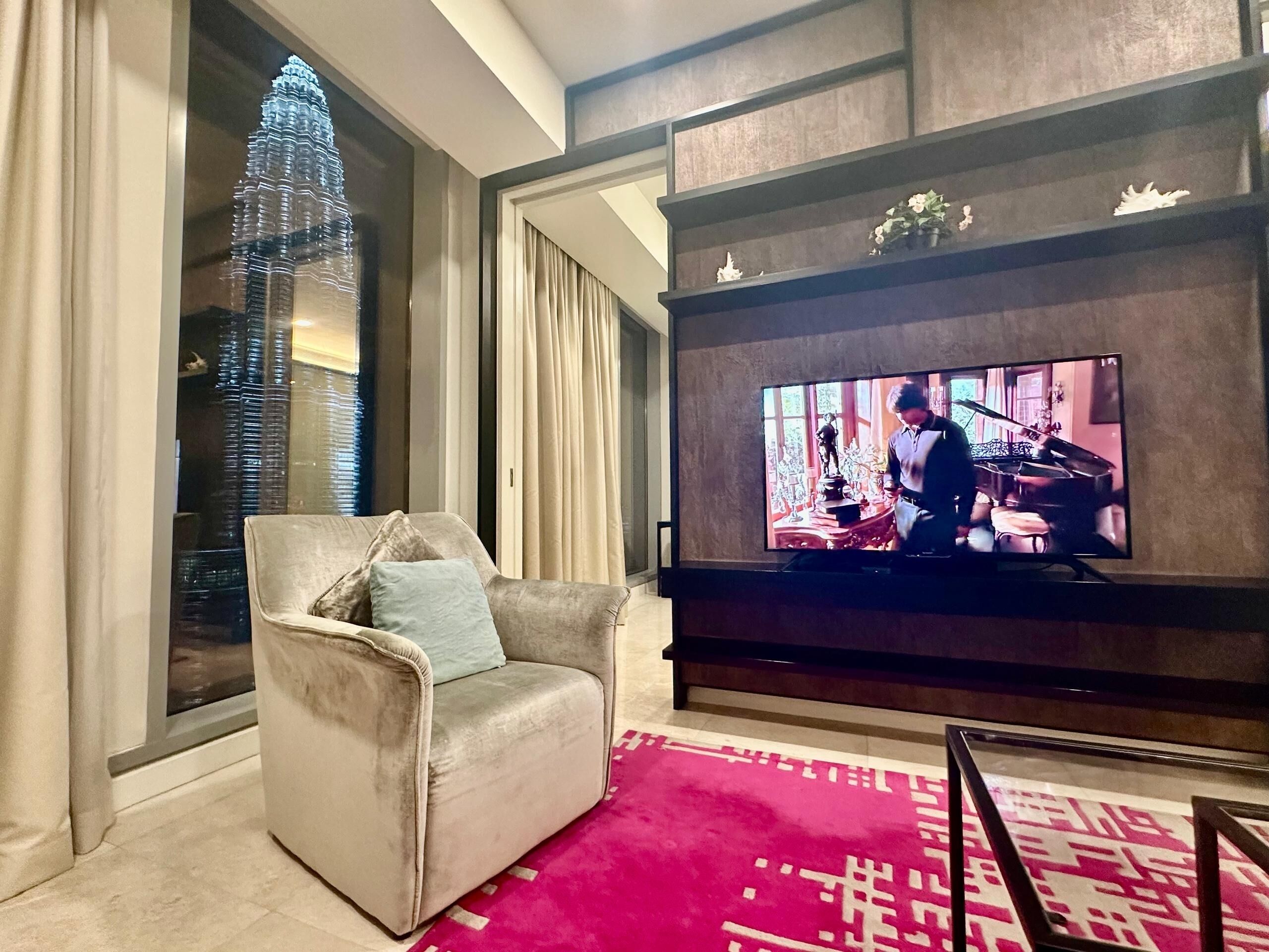 A modern living room with a large flat-screen TV, a plush armchair, and a vibrant red rug.