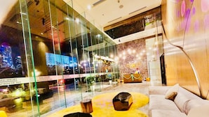 A modern lobby with a glass wall, a reception desk, and a seating area with a yellow patterned rug. - TropicanaThe Residence KLCC By Cozy Stay (Kuala Lumpur)