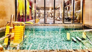 A swimming pool with tiled flooring and yellow floating barriers, surrounded by glass doors leading to a gym area with exercise equipment. - TropicanaThe Residence KLCC By Cozy Stay (Kuala Lumpur)