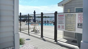 A pool area with a fenced deck, pool rules sign, and a warning sign. - Beautiful 3 Bd condo on 23rd Street with outdoor pool. (Ocean City)