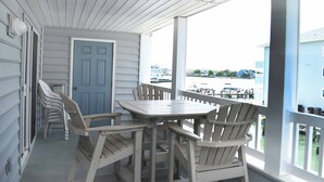 A covered porch with a table and chairs, a door, and a view of a marina with boats. - Beautiful 3 Bd condo on 23rd Street with outdoor pool. (Ocean City)