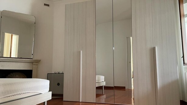 Quarto com chão de madeira, cama, guarda-roupa e espelho.