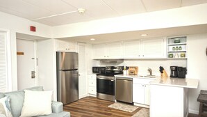 Cocina compacta con armarios blancos, electrodomésticos de acero inoxidable, microondas integrado y cafetera.