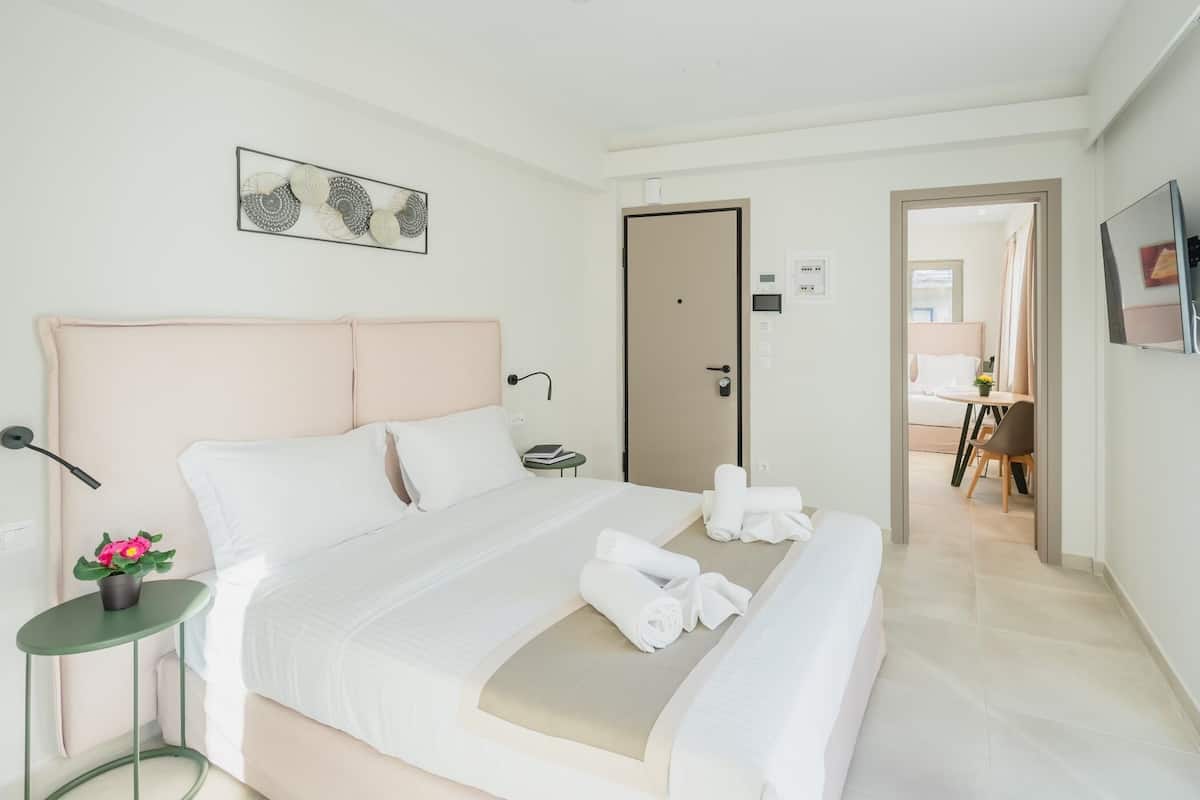 A modern hotel room with a large bed, a bedside table with a lamp, a small plant, and a painting on the wall.
