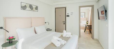 A modern hotel room with a large bed, a bedside table with a lamp, a small plant, and a painting on the wall.