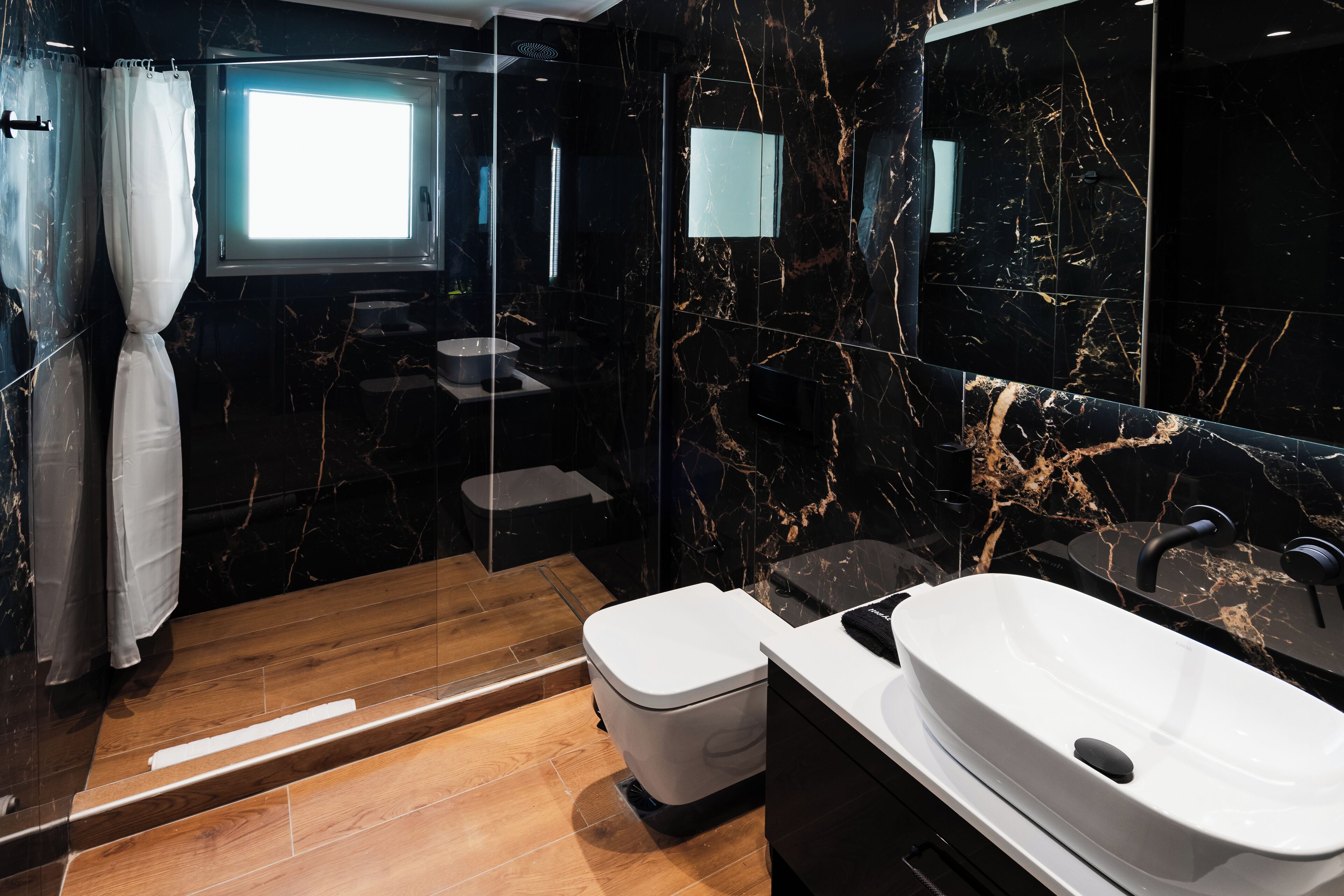 A modern bathroom with a marble floor, a white toilet, a freestanding bathtub, and a large mirror.