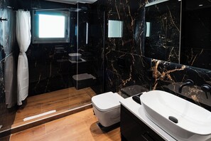 Un baño moderno con piso de mármol, inodoro blanco, tina independiente y un espejo grande.
