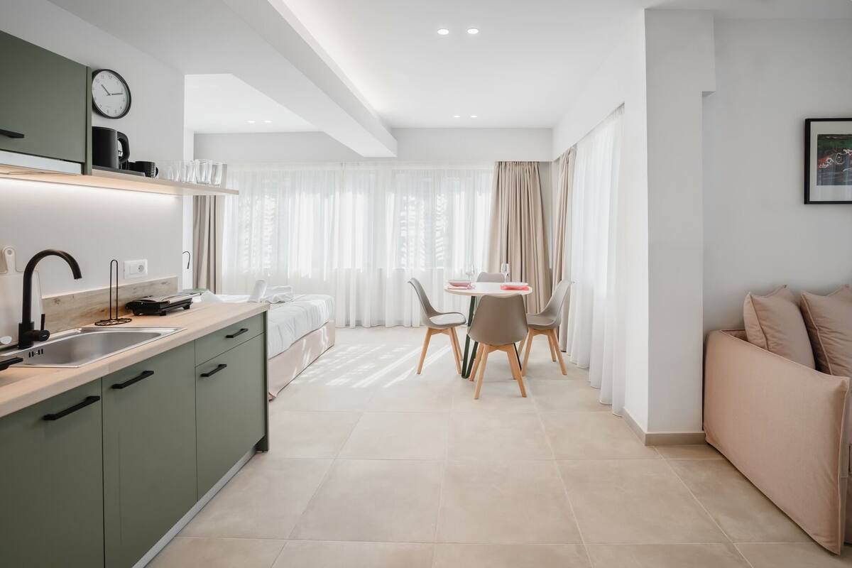A modern kitchen with a dining area, a sofa, and a window with curtains.