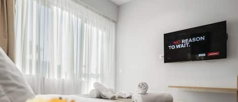 Una habitación de hotel moderna con una cama grande, un televisor de pantalla plana montado en la pared y una ventana con cortinas traslúcidas.