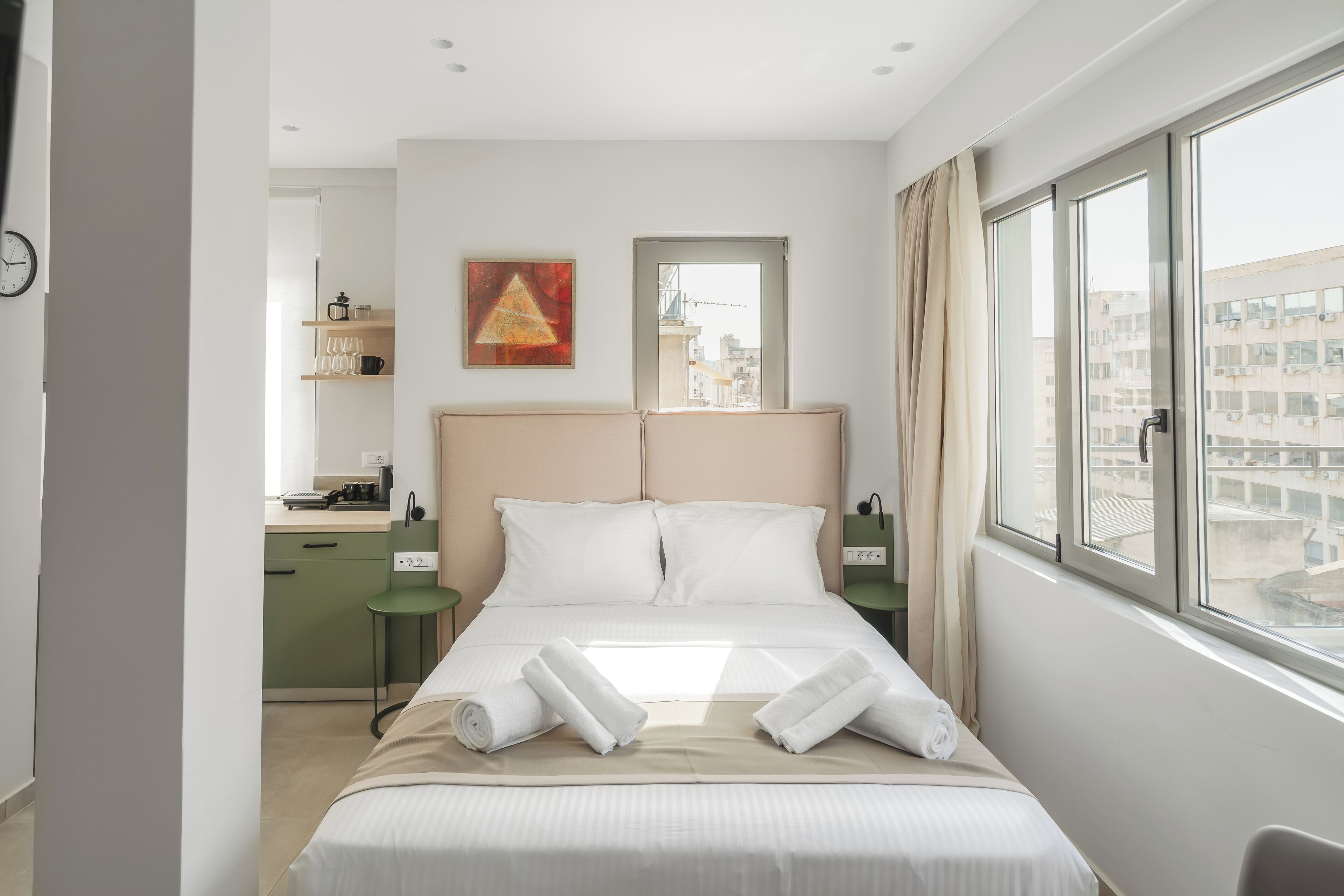 A hotel room with a large bed, a desk, a chair, a nightstand, a mirror, a window, and a view of buildings outside.