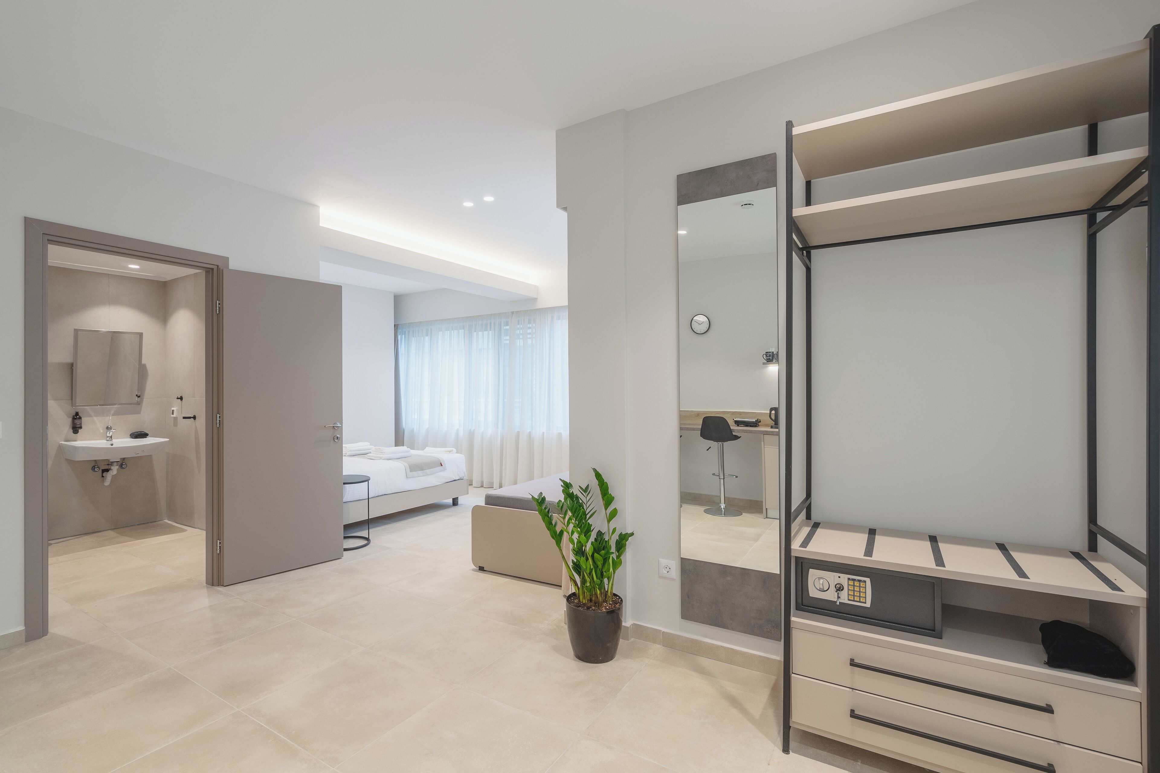 A modern hotel room with a large bed, a bedside table, a mirror, a wardrobe, and a potted plant.