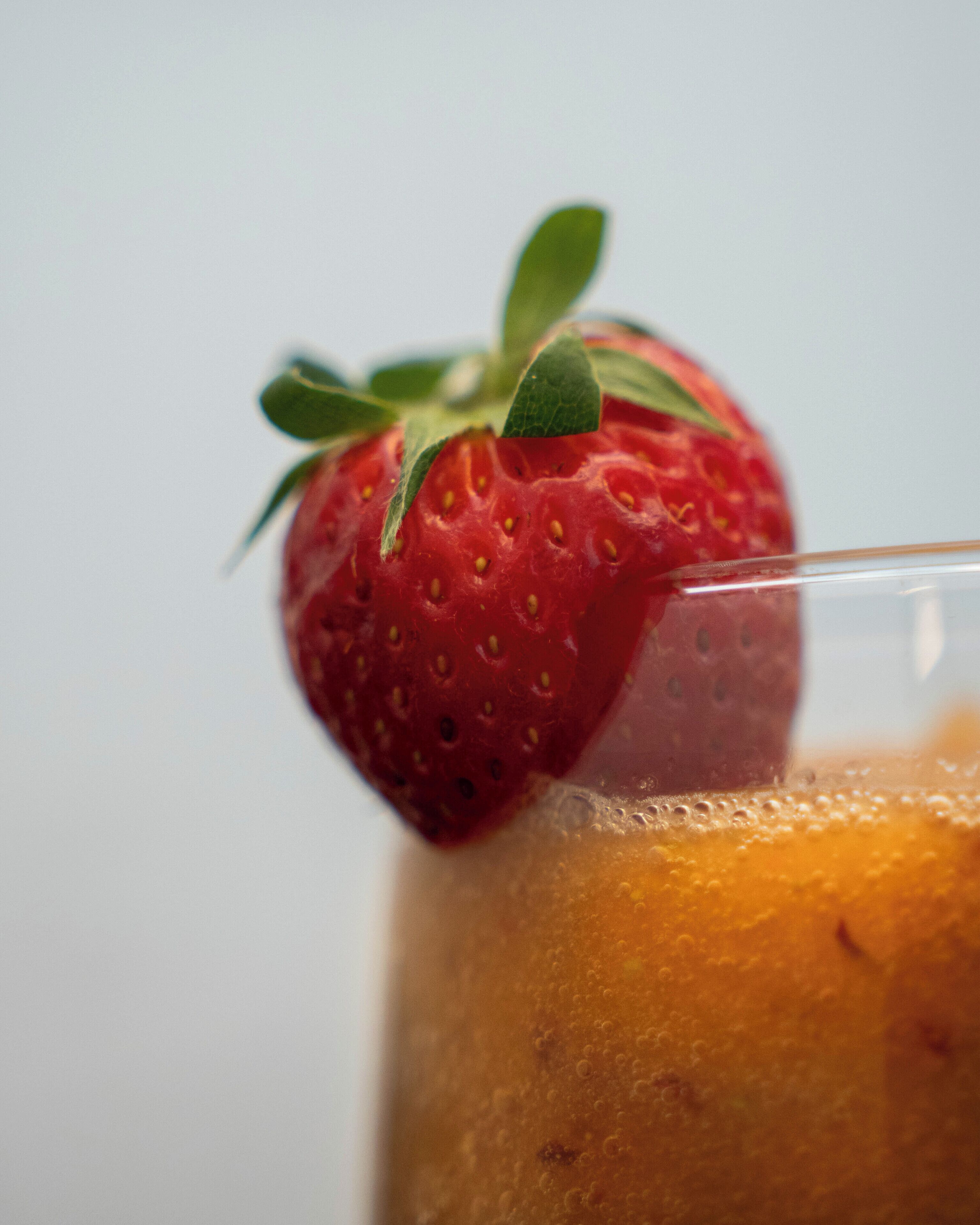 A close-up of a strawberry on a glass of orange juice.