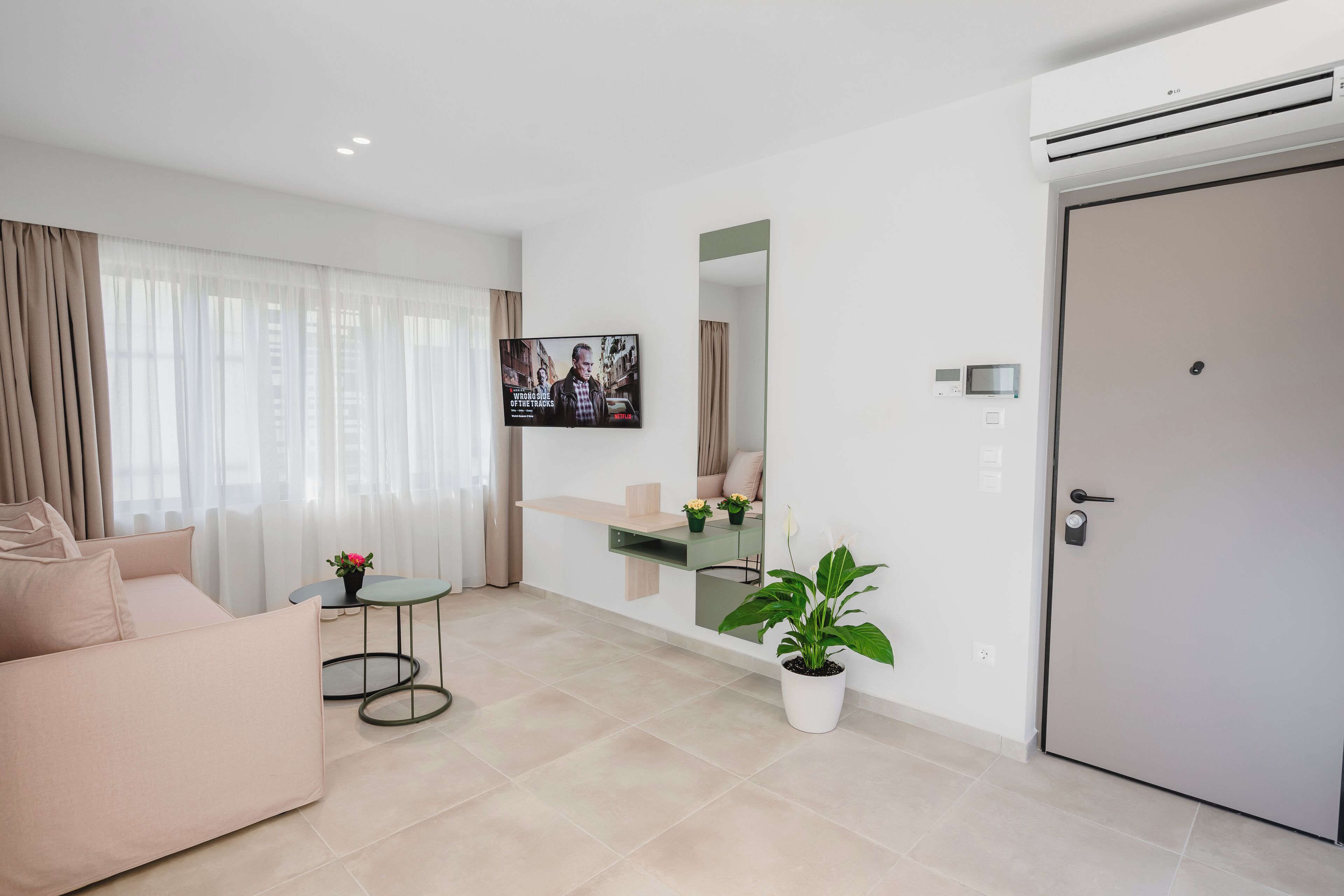 A modern living room with a sofa, a small table with a plant, a TV mounted on the wall, and a door.