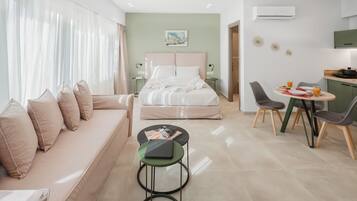 Una habitación de hotel moderna con cama, sofá, mesa de comedor con sillas y una pequeña cocina.