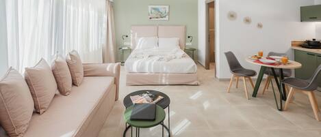 Una habitación de hotel moderna con cama, sofá, mesa de comedor con sillas y una pequeña cocina.