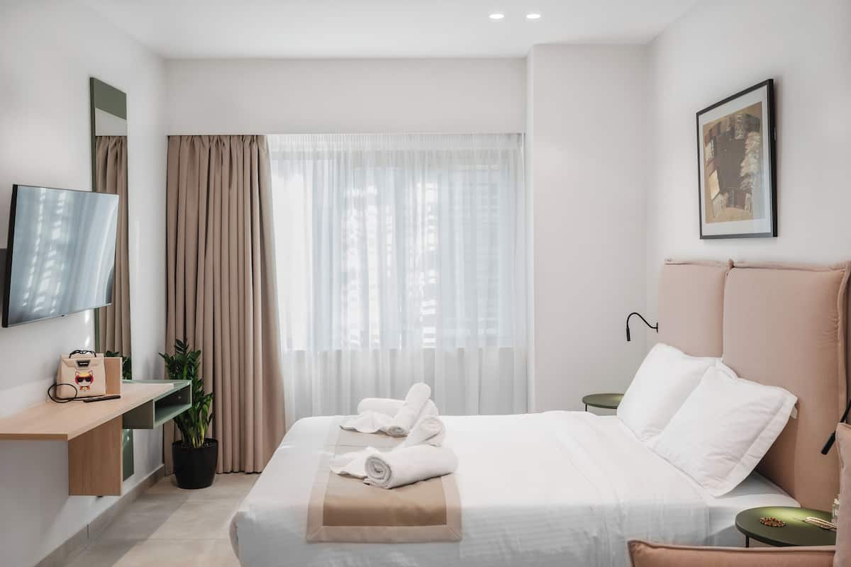 A modern hotel room with a bed, a desk, a TV, and a window with curtains.