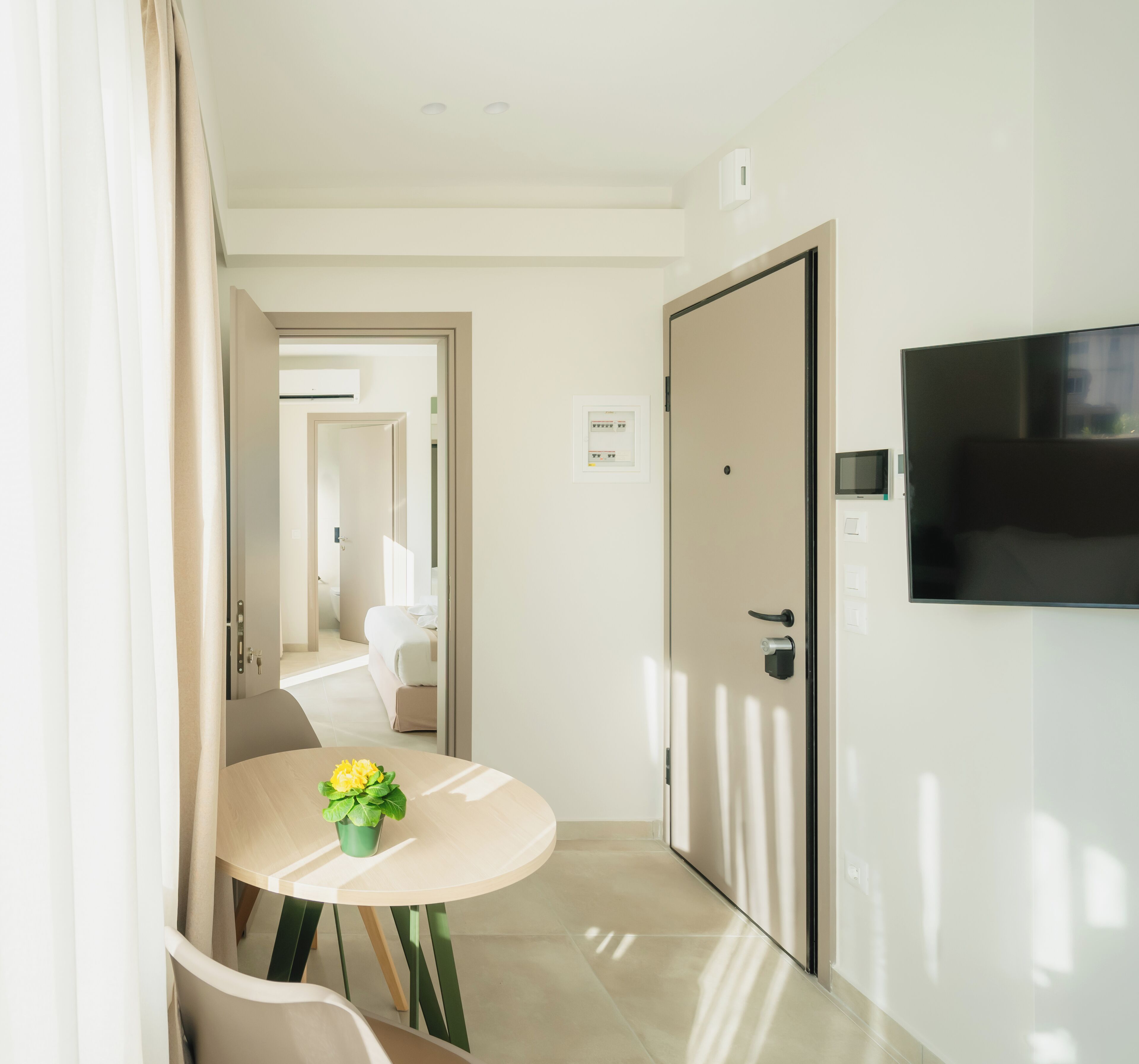 A hotel room with a bed, a TV mounted on the wall, and a small table with a flower vase.