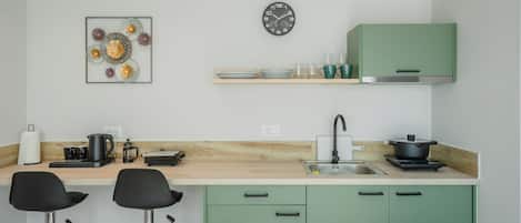 A modern kitchen with green cabinets, a wooden countertop, a black clock, and a decorative wall piece.