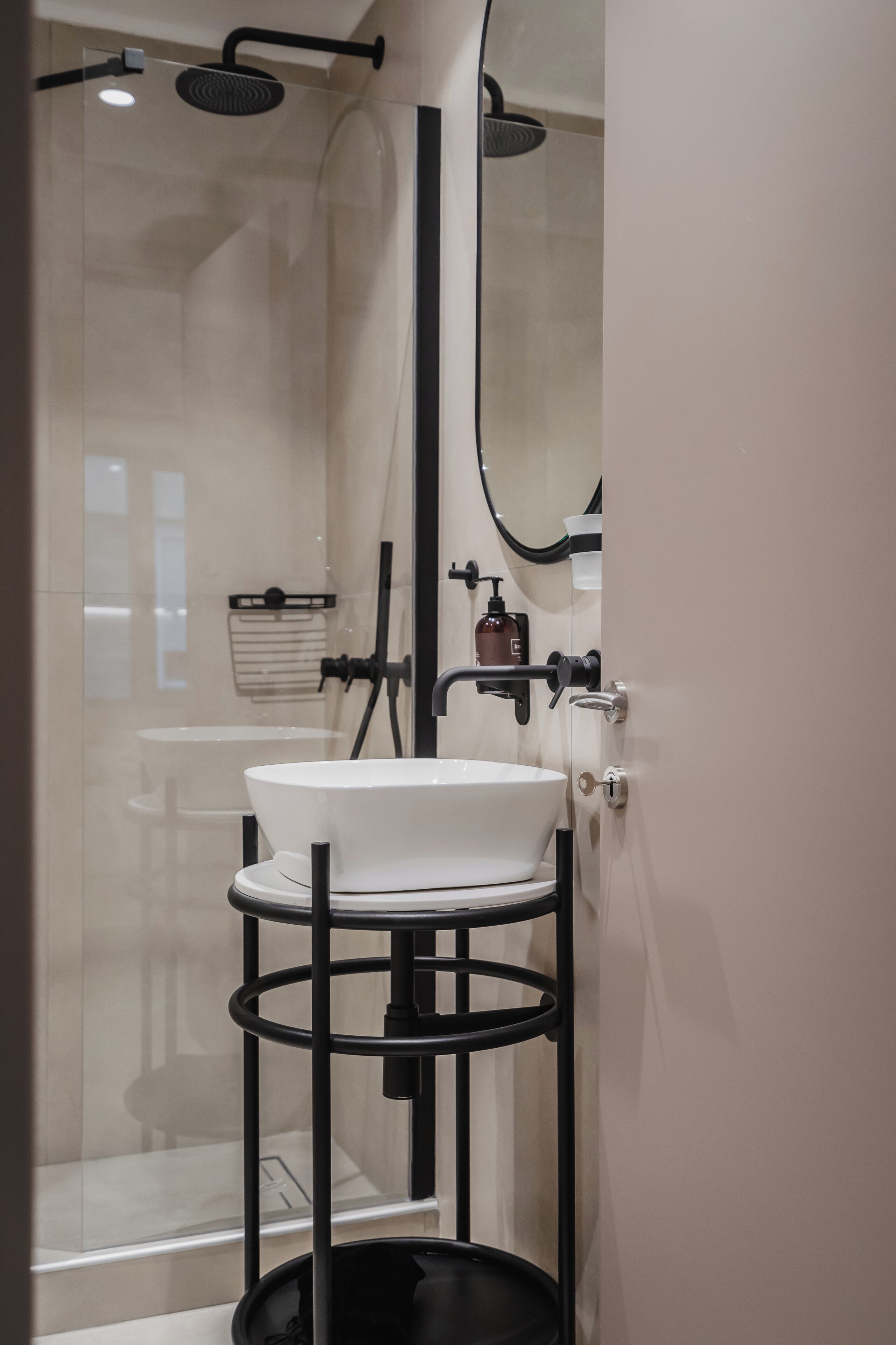 Une salle de bain moderne avec une douche à parois de verre, un lavabo blanc posé sur un support en métal noir et un miroir au-dessus du lavabo.
