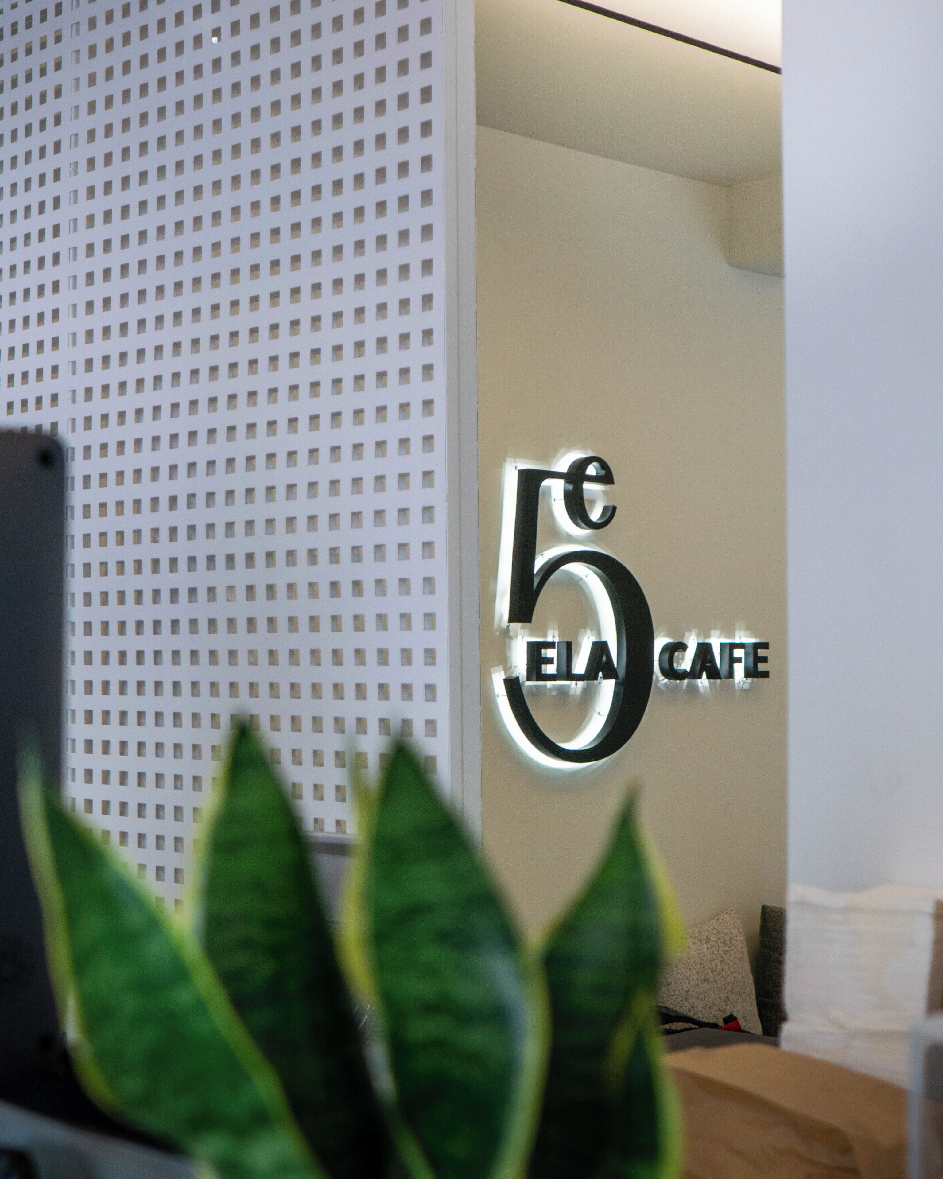 Ett välkomnande område med modern design, med en väggmonterad skylt som visar texten "5 ELA CAFE".