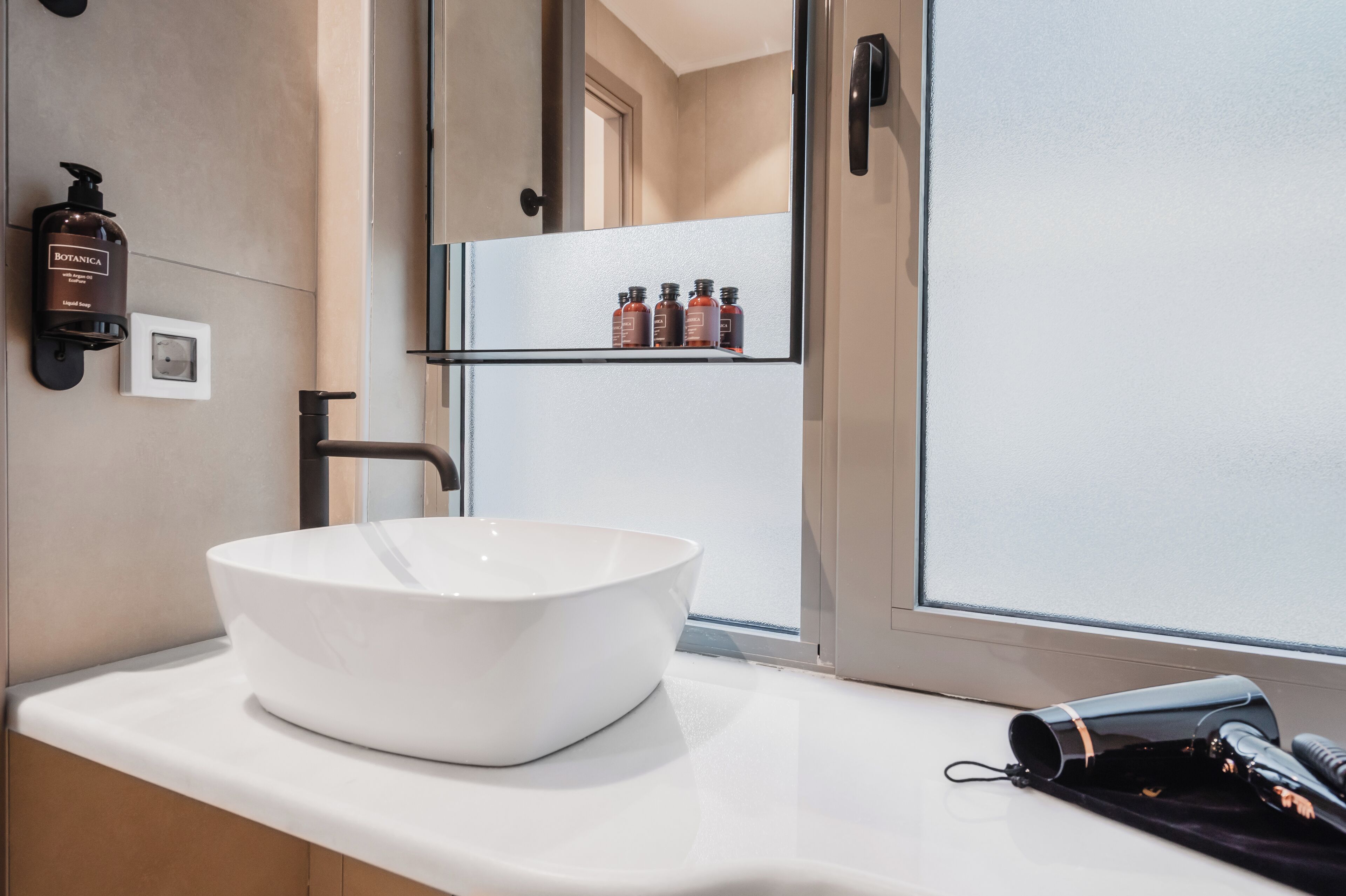 A modern bathroom with a large white sink, a handheld showerhead, and a hairdryer on the counter.