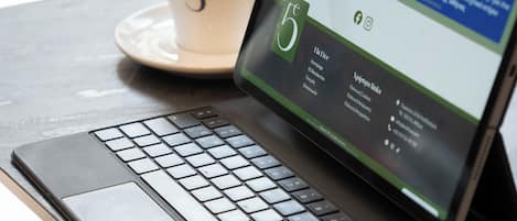 Una computadora portátil sobre una mesa, con una taza etiquetada '5' a su lado.